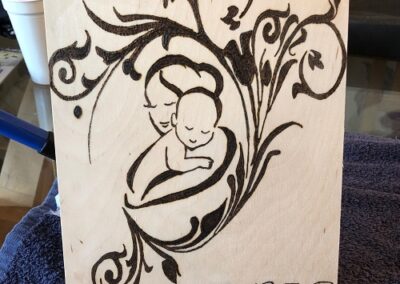 A mother and child, burned into A4 wood and surrounded with a floral design.